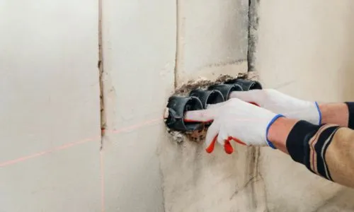 Elektricien met werkhandschoenen plaatst inbouwdozen in een wand
